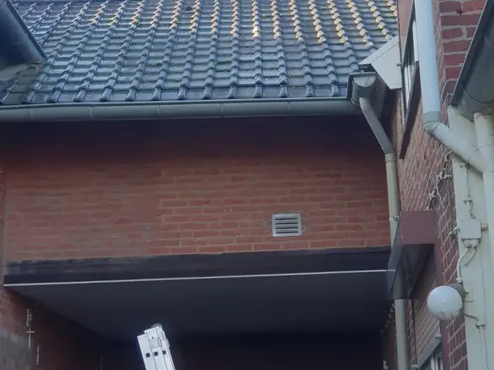 Hellend pannendak van een aanbouw met nieuwe zinken goot langs een bakstenen gevel