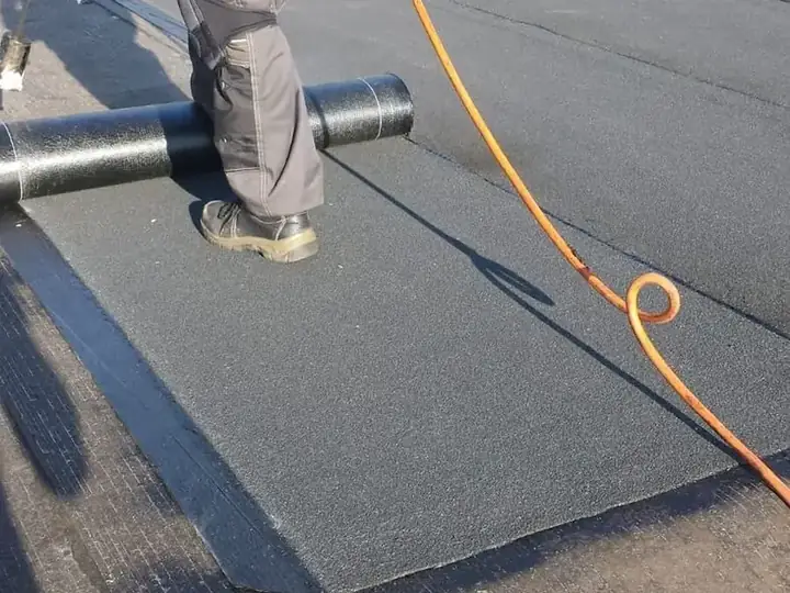 Dakdekker rolt en brandt dakbedekking aan op een plat dak, met de gasslang naast zich