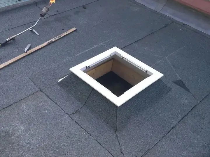 Plat dak met een uitgezaagde sparing voor een lichtkoepel en gereedschap ernaast